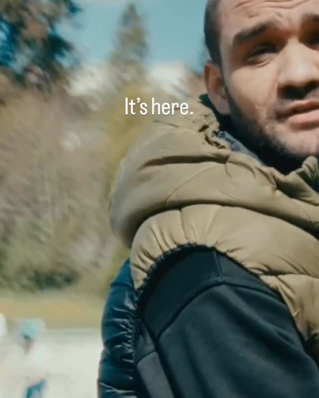 Dusan outdoors in a quilted vest, looking at the camera, with the text “It’s here.”