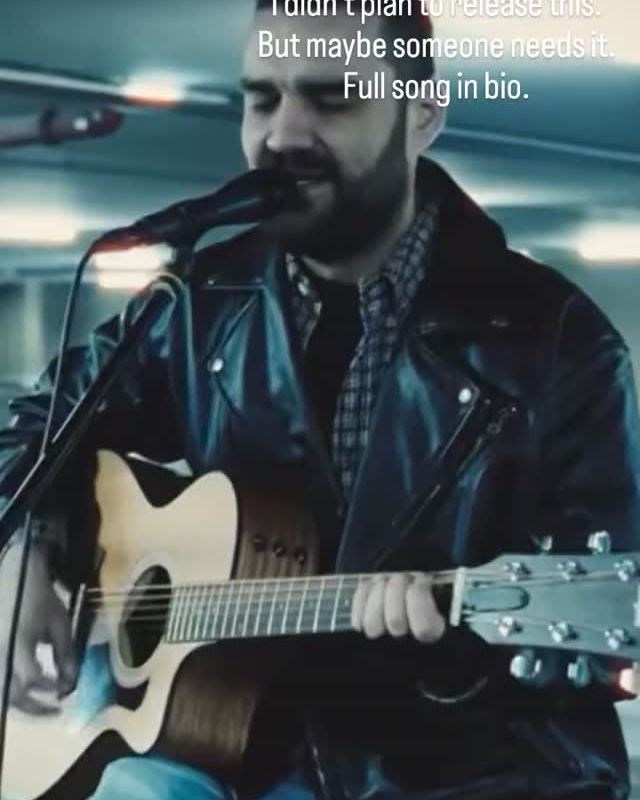 Dusan singing and playing an acoustic guitar in a bright, modern hall