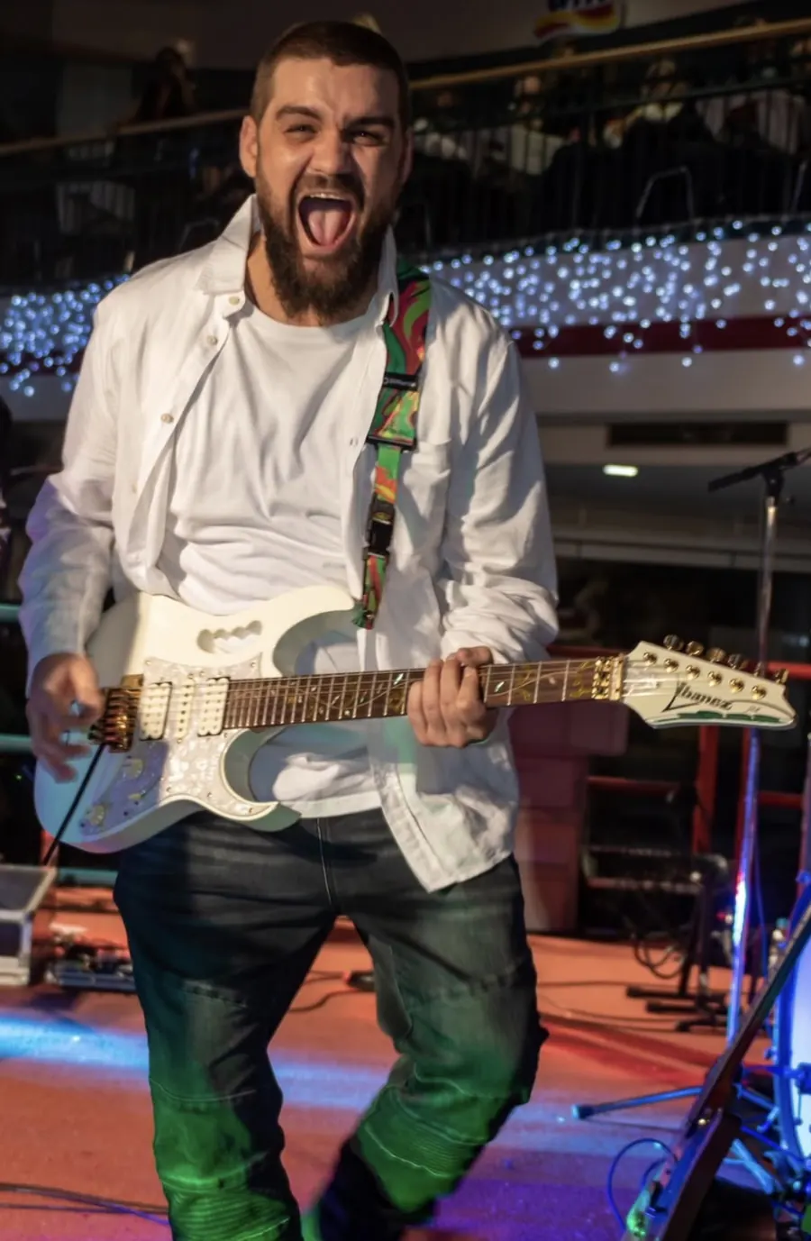 Dusan playing a white electric guitar and singing live on a stage